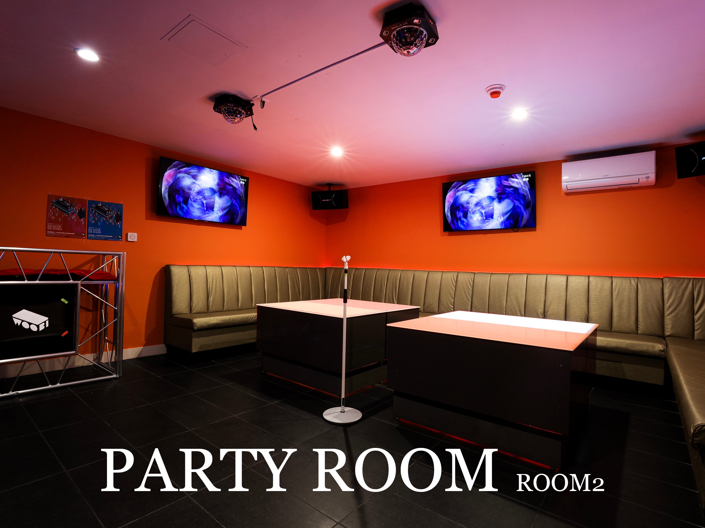 Woobi's spacious party room with orange walls, lounge seating, karaoke screens, and two tables
